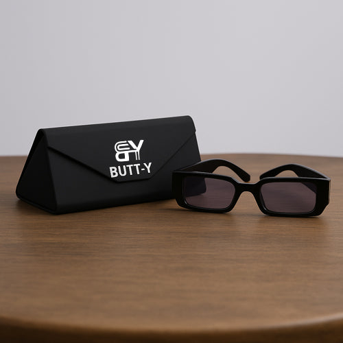 Black sunglasses and black case with 'EVY BUTT-Y' branding on a wooden surface.