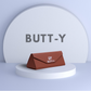 Brown pouch with 'BUTT-Y' branding on a white platform against a light gray background